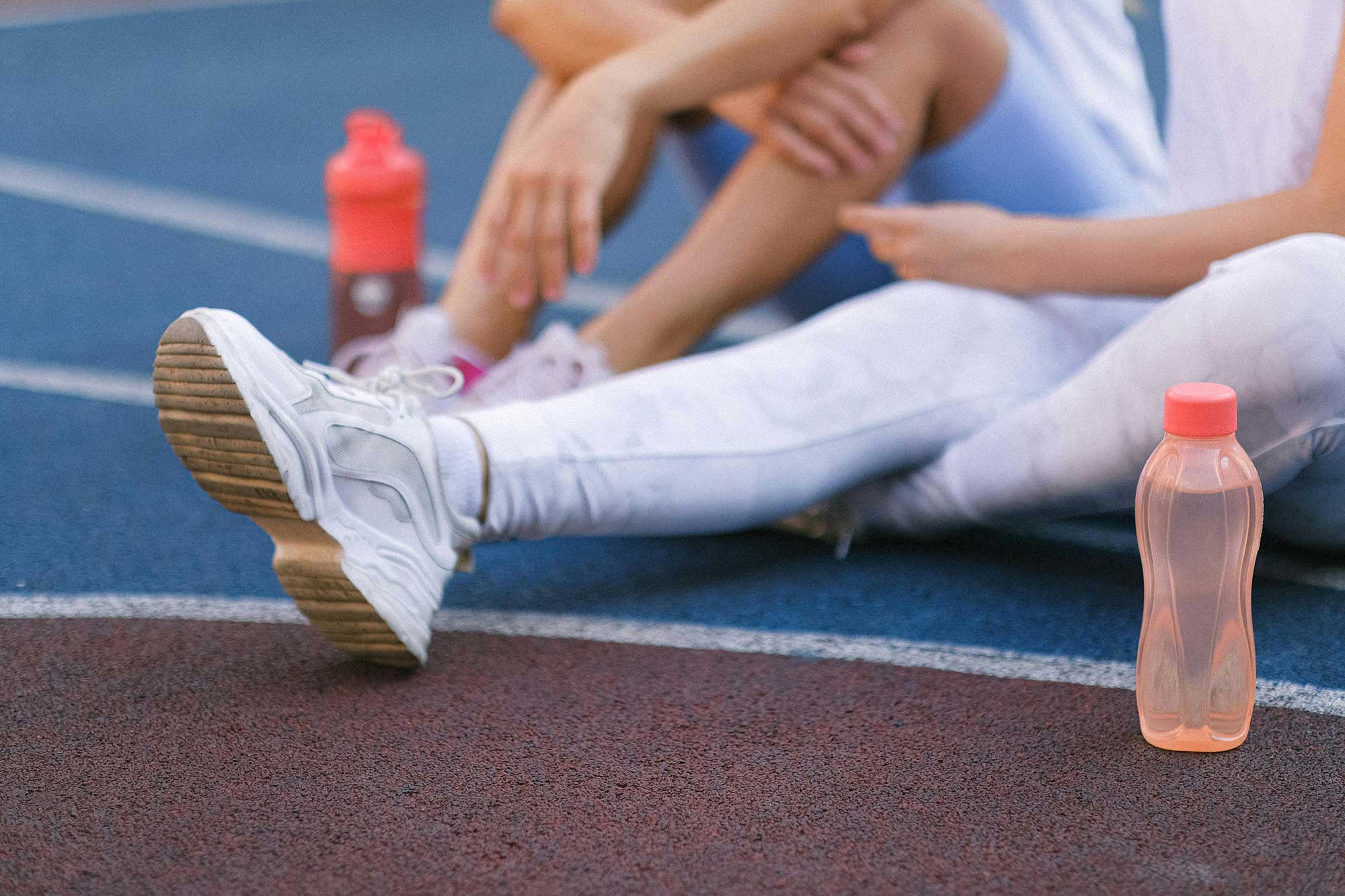 Runner stretching on track with water bottle, reinforcing SPF use before training.