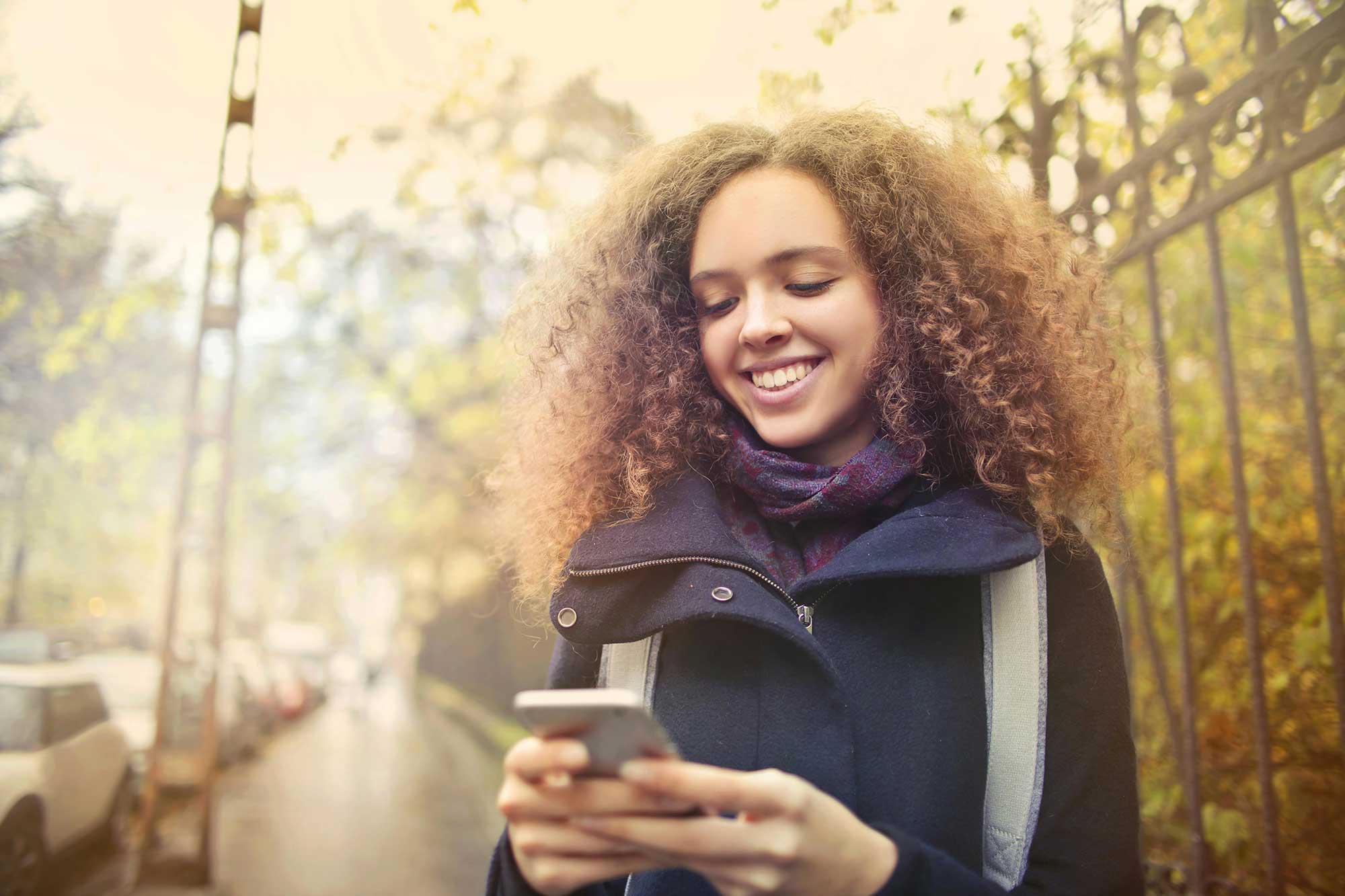 Smiling woman walking outdoors with phone, showing importance of SPF for commuters in the city.