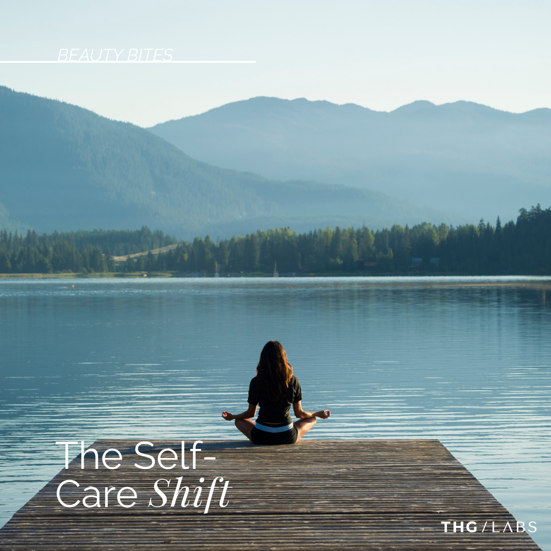 Person seated in quiet meditation by a lake, reflecting the shift towards intentional self-care rituals