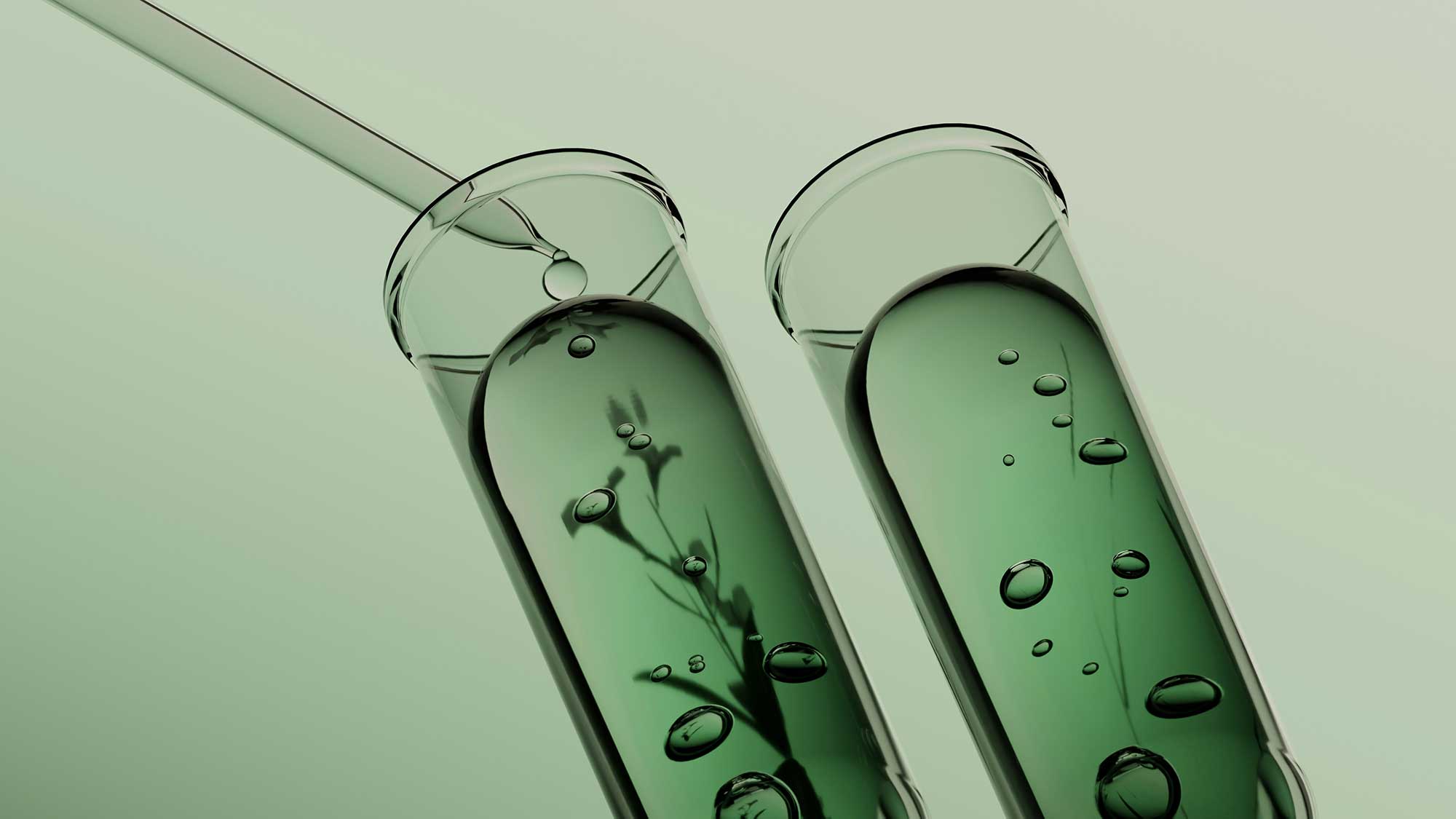 Laboratory test tubes containing green cosmetic formulation liquid with botanical silhouettes, representing biotech beauty manufacturing and sustainable ingredient innovation at THG LABS.