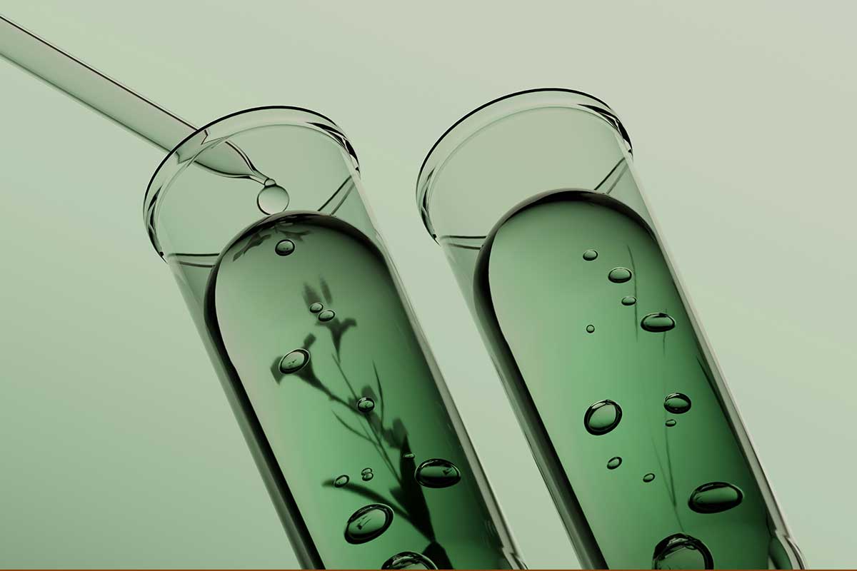 Laboratory test tubes containing green cosmetic formulation liquid with botanical silhouettes, representing biotech beauty manufacturing and sustainable ingredient innovation at THG LABS.